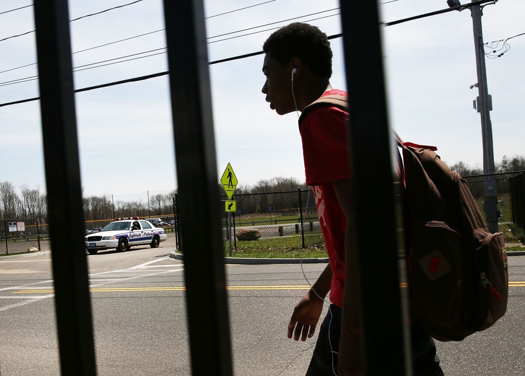 A teenage boy walks across the street from a Suffolk County police car.