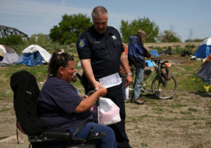 A police officer hands out eviction notices to residents at a homeless tent city in Sacramento, CA