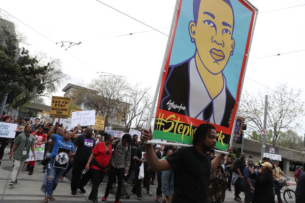 Photo of a Black Lives Matter protest. One activist holds a giant poster featuring Stephon Clark.