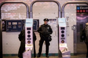 A New York police officer stands just beyond a Metrocard swipe turnstile