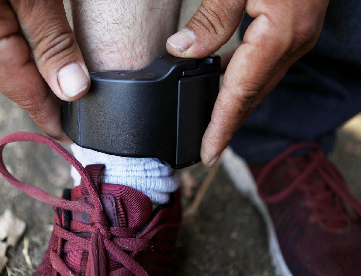A migrant father from Guatemala, who chose not to be identified, demonstrates the ankle monitor he is required by ICE to wear 24 hours a day
