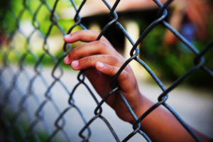 A child's hand touches a chain-link fence