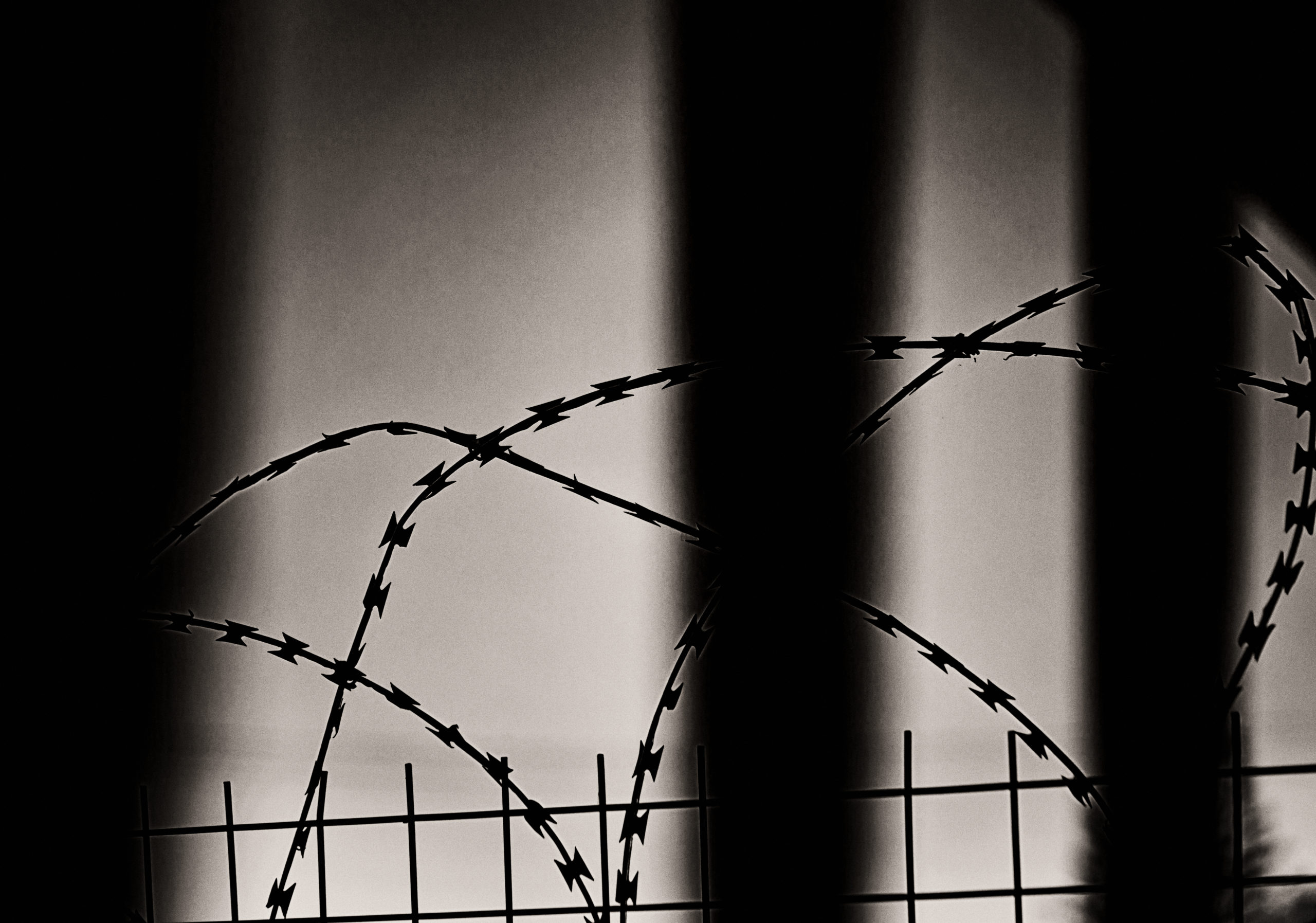 Sharp barbed razor wire fence seen through prison bars
