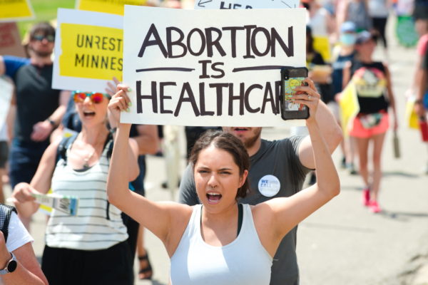 A woman stands at an abortion-rights protest holding a sign that reads "abortion is healthcare."