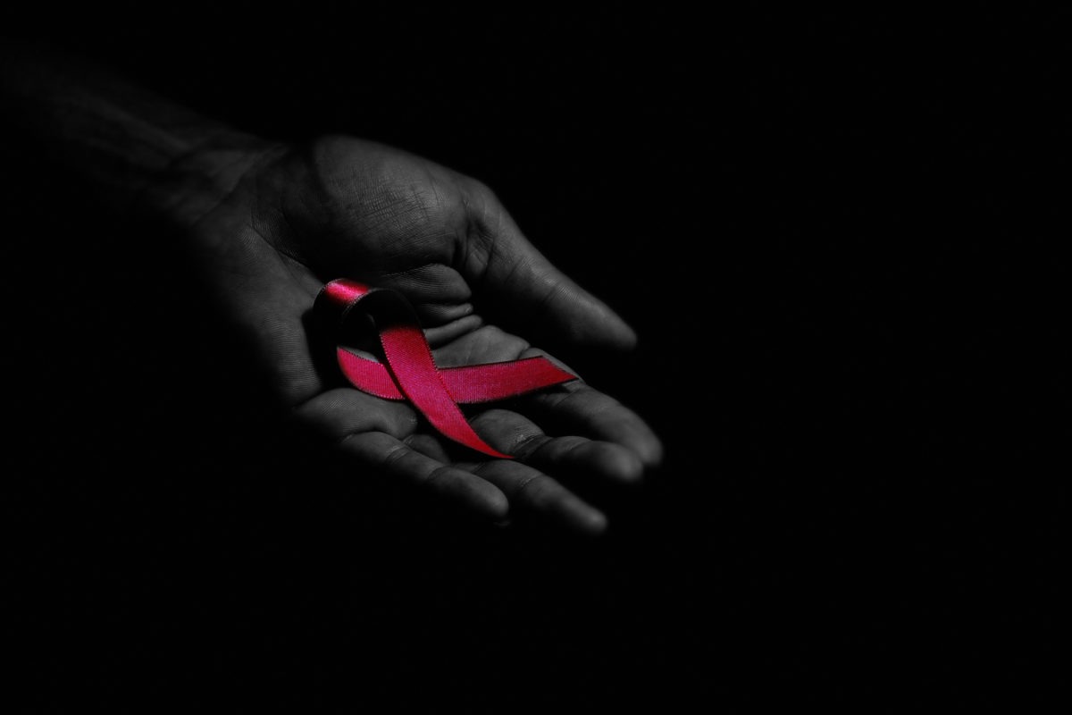 A hand holding a red HIV/AIDS ribbon.