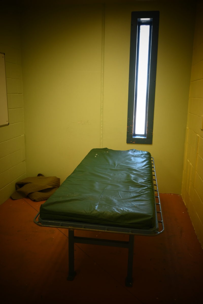 This photo shows the thin green vinyl mattress and thin, small window in the room where people are detained.