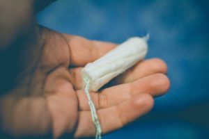 This photo shows a hand holding an unused tampon set over a blue background.
