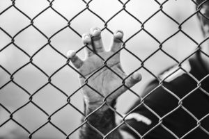 This photo shows a man's hand holding onto a chain-link fence. His face is not shown.
