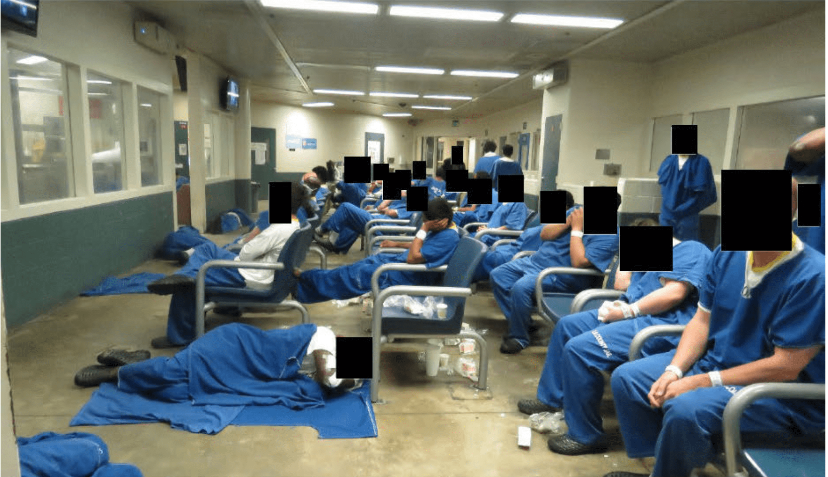 This photo shows Los Angeles County's Inmate Reception Center. Men sit in blue jumpsuits either in chairs or sleeping on a concrete floor. Garbage sits on the floor as well. The faces are censored.