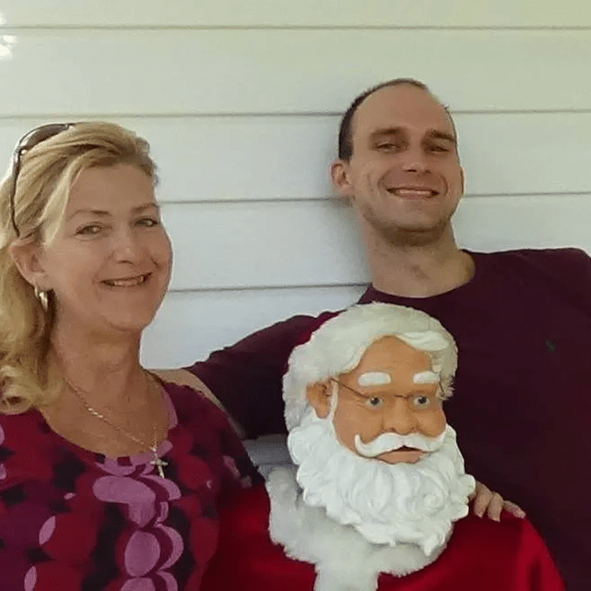 Rhonda McLemore (left) and Joshua McLemore (right) smiling at the camera during Christmas time. A Santa Claus statue stands between them.