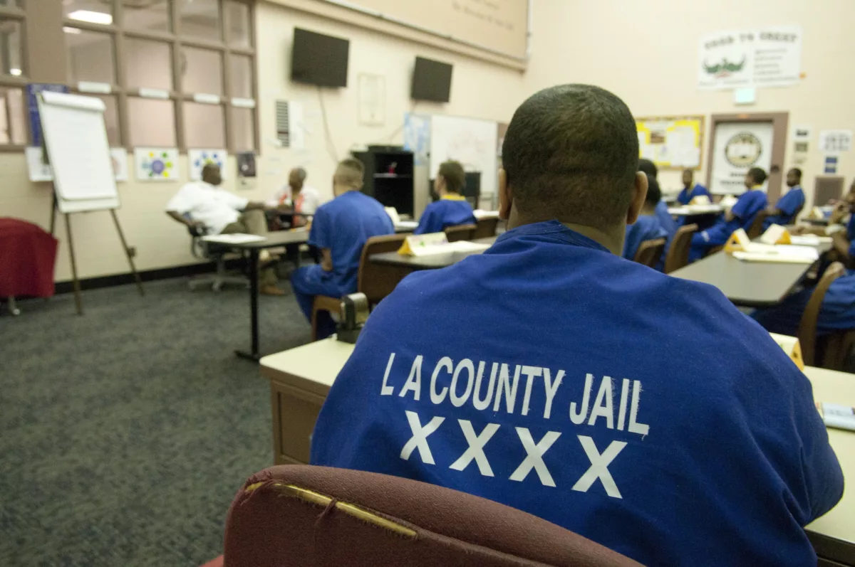 This photo shows a man in a blue jumpsuit whose back says "Los Angeles County Jail." His face cannot be seen.