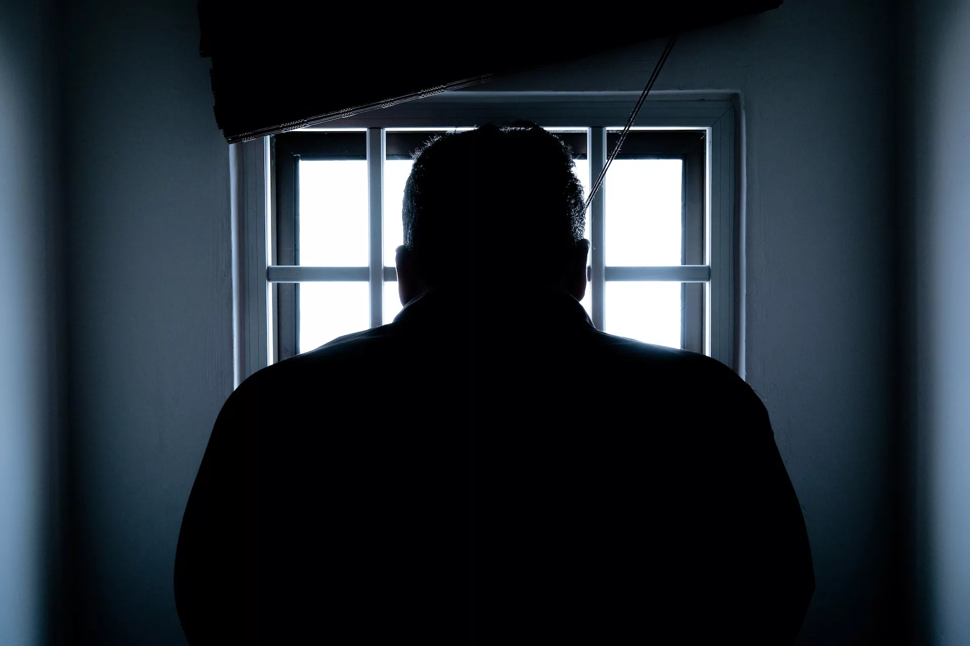 This photo shows the black silhouette of a man from behind staring out a window.