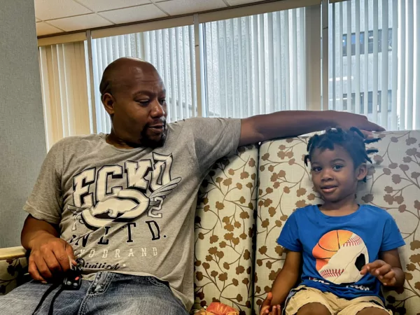 This photo shoes Quintin Walls (left) and his young son (right) sitting on a floral couch.