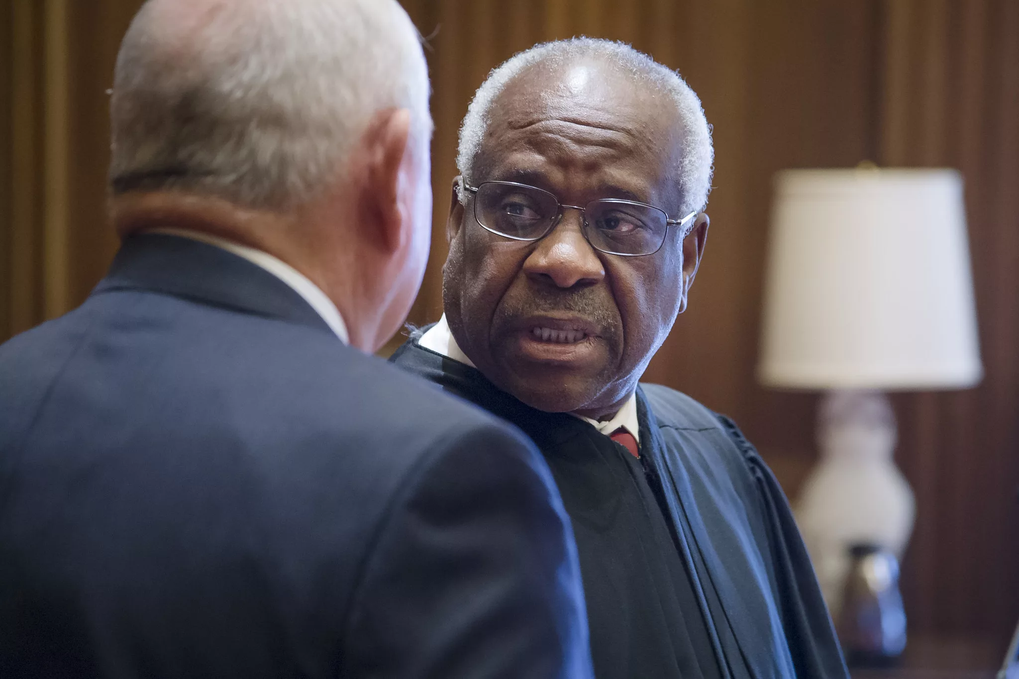 This photo shows a close-up of U.S. Supreme Court Justice Clarence Thomas. He is speaking to former U.S. Secretary of Agriculture Sonny Perdue, whose back is turned to the camera.
