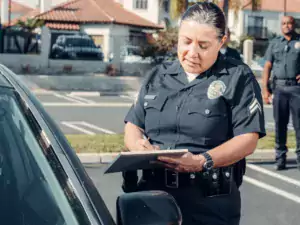 This is a stock photo of a policewoman who has pulled over a driver. She is standing talking to an open driver's window as she holds a clipboard.