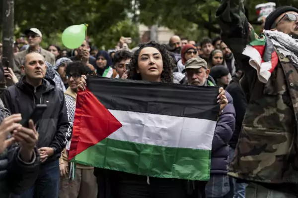This photo shows a woman at a protest holding a Palestinian flag across her chest.