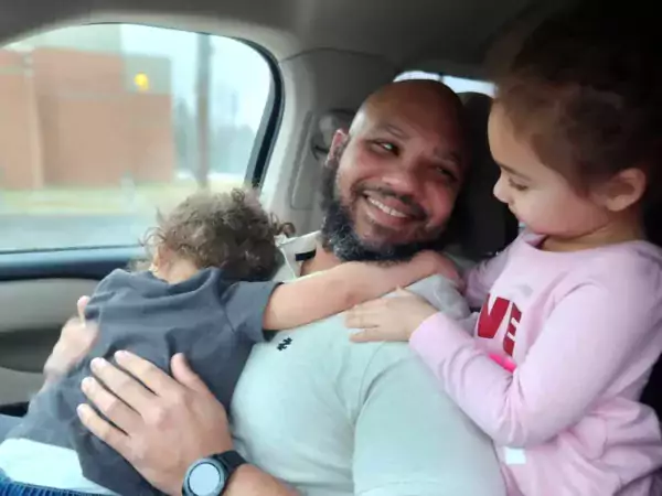 Two children inside a car hug their smiling dad, who was just released from the St. Clair County Jail