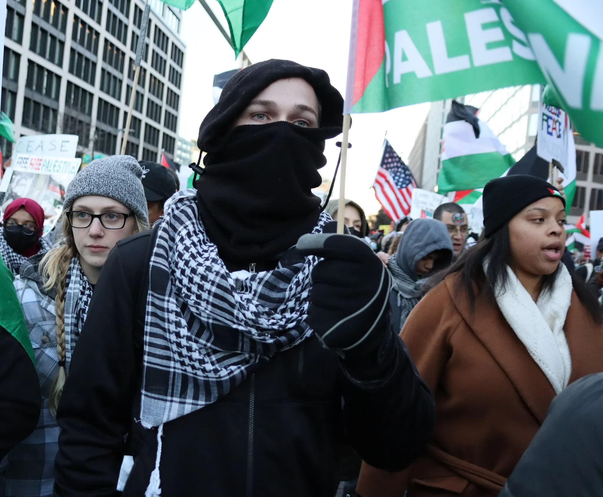 This photo shows a protester wearing a black mask over his nose and mouth, while holding a Palestinian flag.