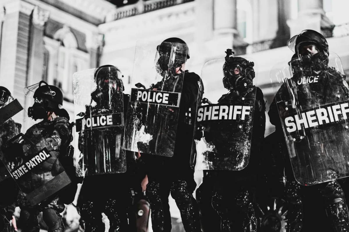 This photo shows a line of riot cops holding shields and wearing helmets.