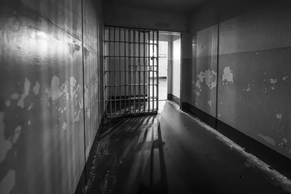 Black and white photo of an empty jail cell with an open door.