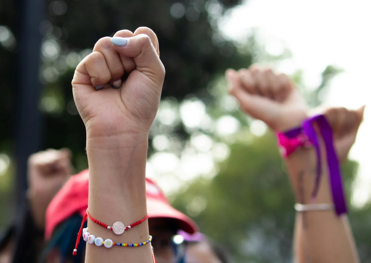 This photo shows a close up of multiple people with raised fists at a protest outdoors.