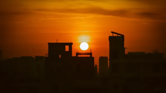 A silhouette of buildings with the sun in the background.