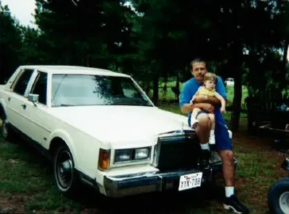 Robert Roberson sits on the hood of a 1980s car holding his infant daughter, Nikki.