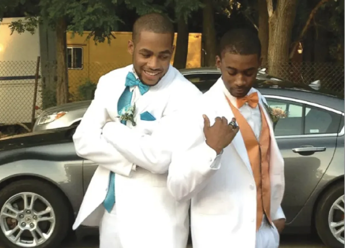 Timothy Jones (left) stands in a white tuxedo next to a friend.