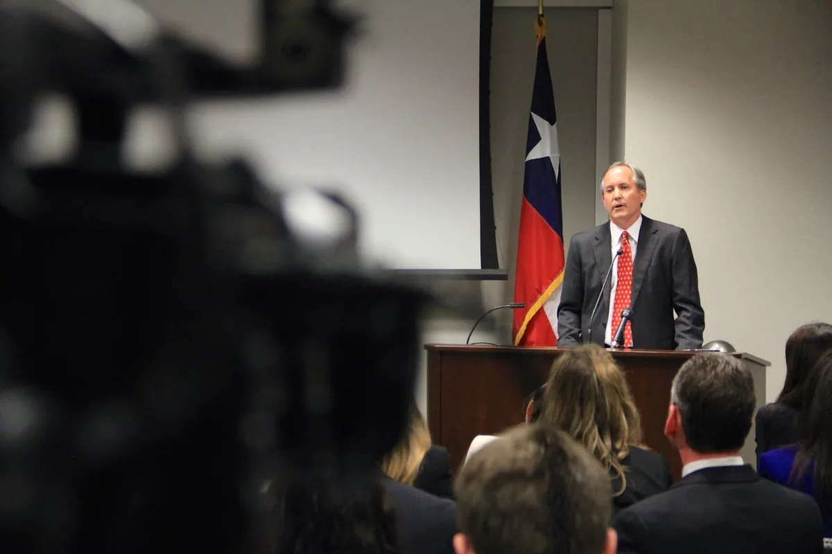 This photo shows Texas Attorney General Ken Paxton speaking at a lectern at a press conference.