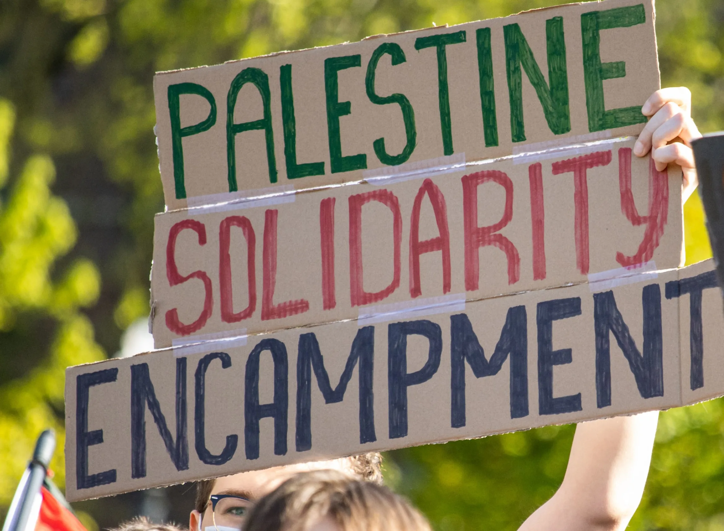 This is a photo of a student holding a sign that reads, "Palestine Solidarity Encampment."