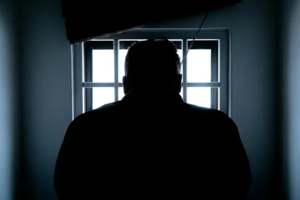 This photo shows a silhouette of the back of a man's head. He peers out of a prison cell window.