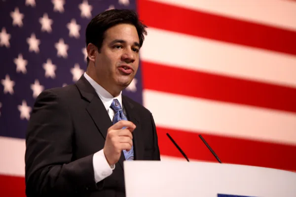 This photo shows Idaho Attorney General Raúl Labrador speaking at a lectern in front of an American flag.