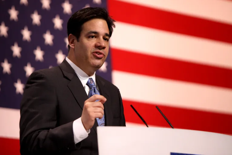 This photo shows Idaho Attorney General Raúl Labrador speaking at a lectern in front of an American flag.