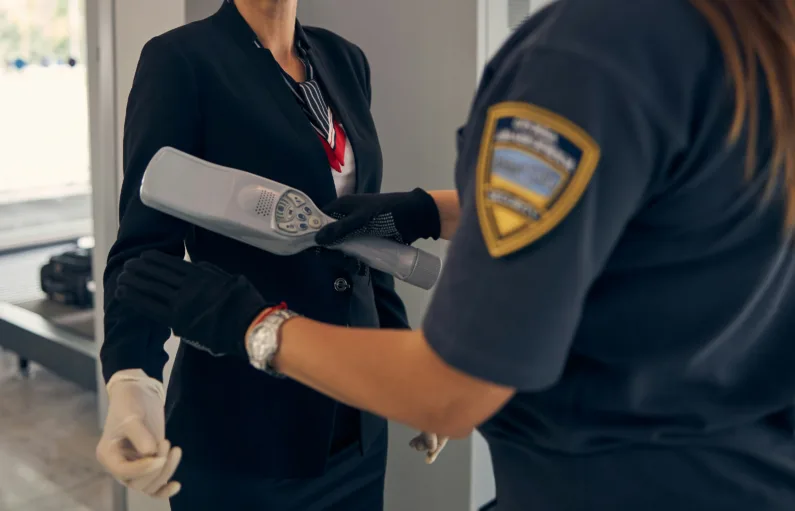 This photo shows a secuity guard waving a wand-sized metal detector over a woman's body.