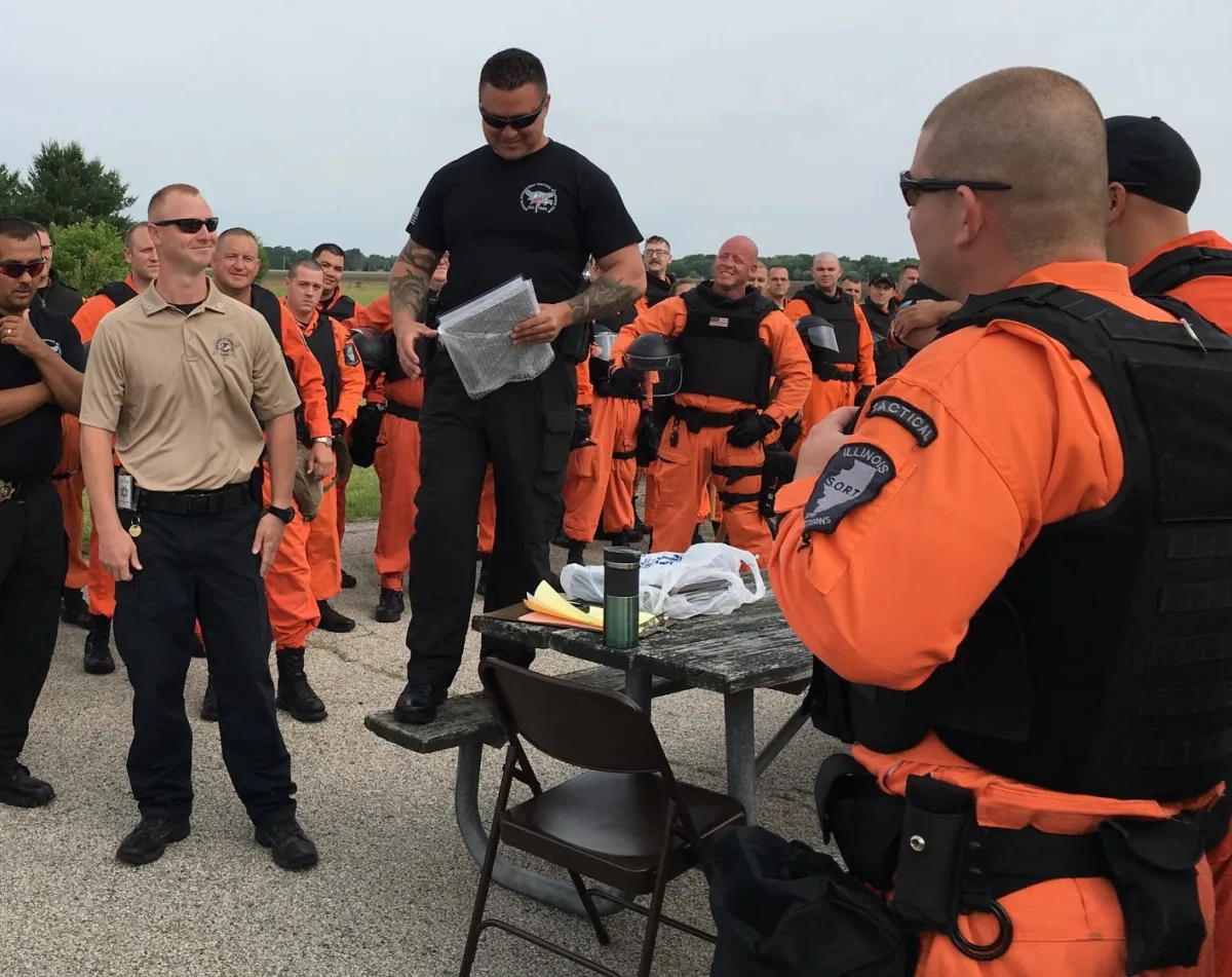 This photo shows Illinois Department of Corrections Special Operations Response Team (SORT) standing outdoors in orange jumpsuits.