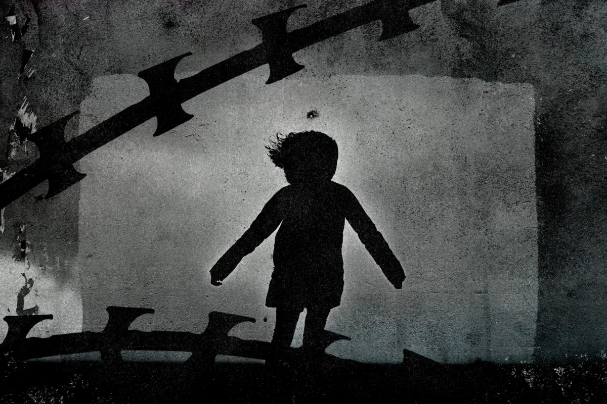 Silhouette of child and razor wire over concrete