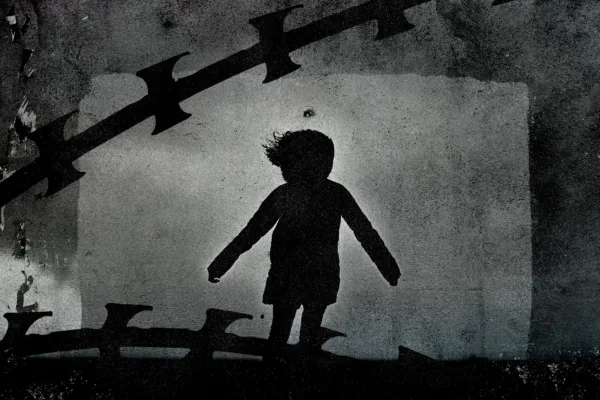 Silhouette of child and razor wire over concrete
