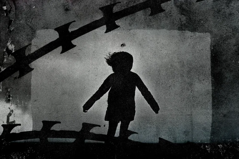 Silhouette of child and razor wire over concrete