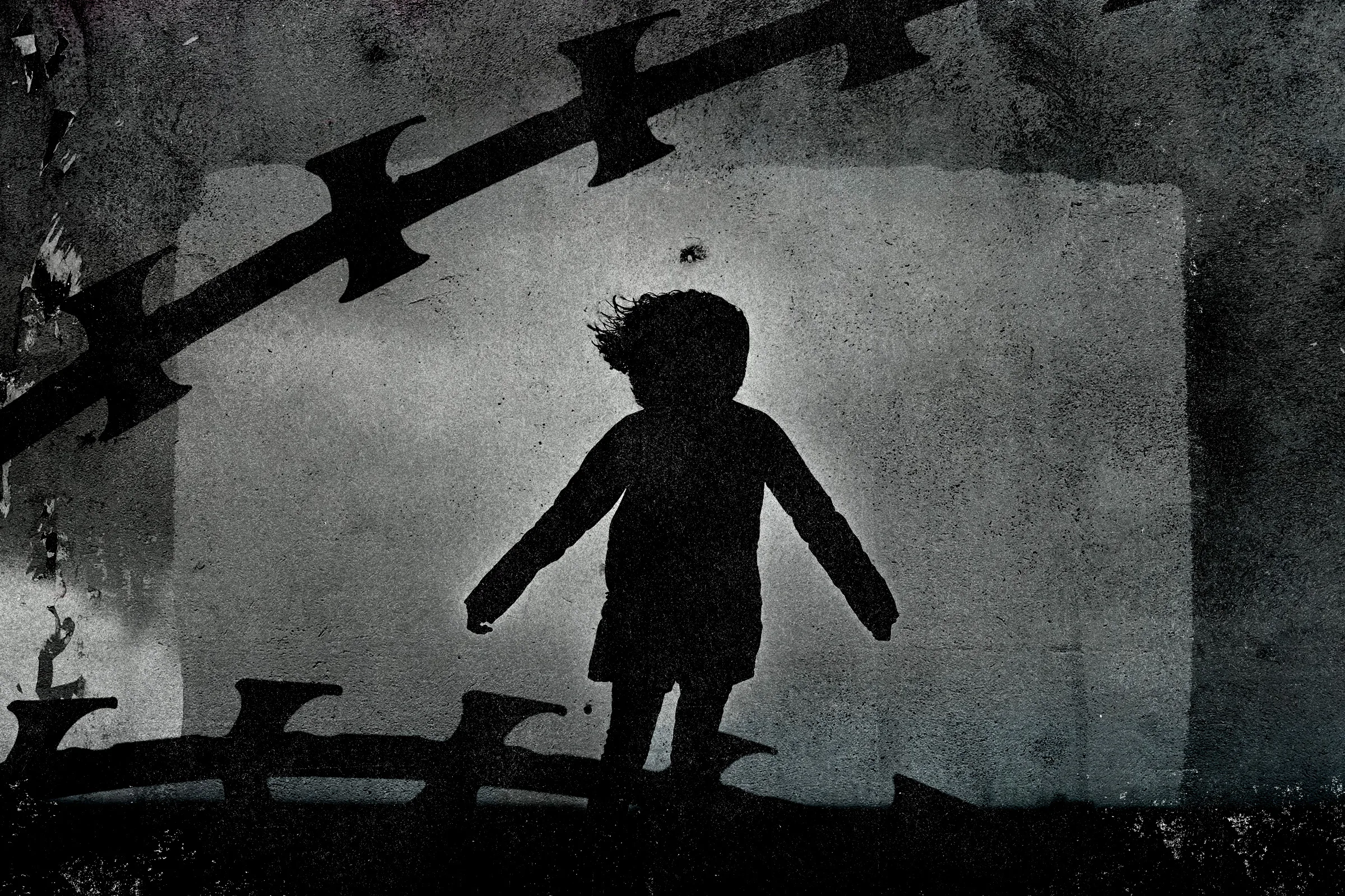 Silhouette of child and razor wire over concrete