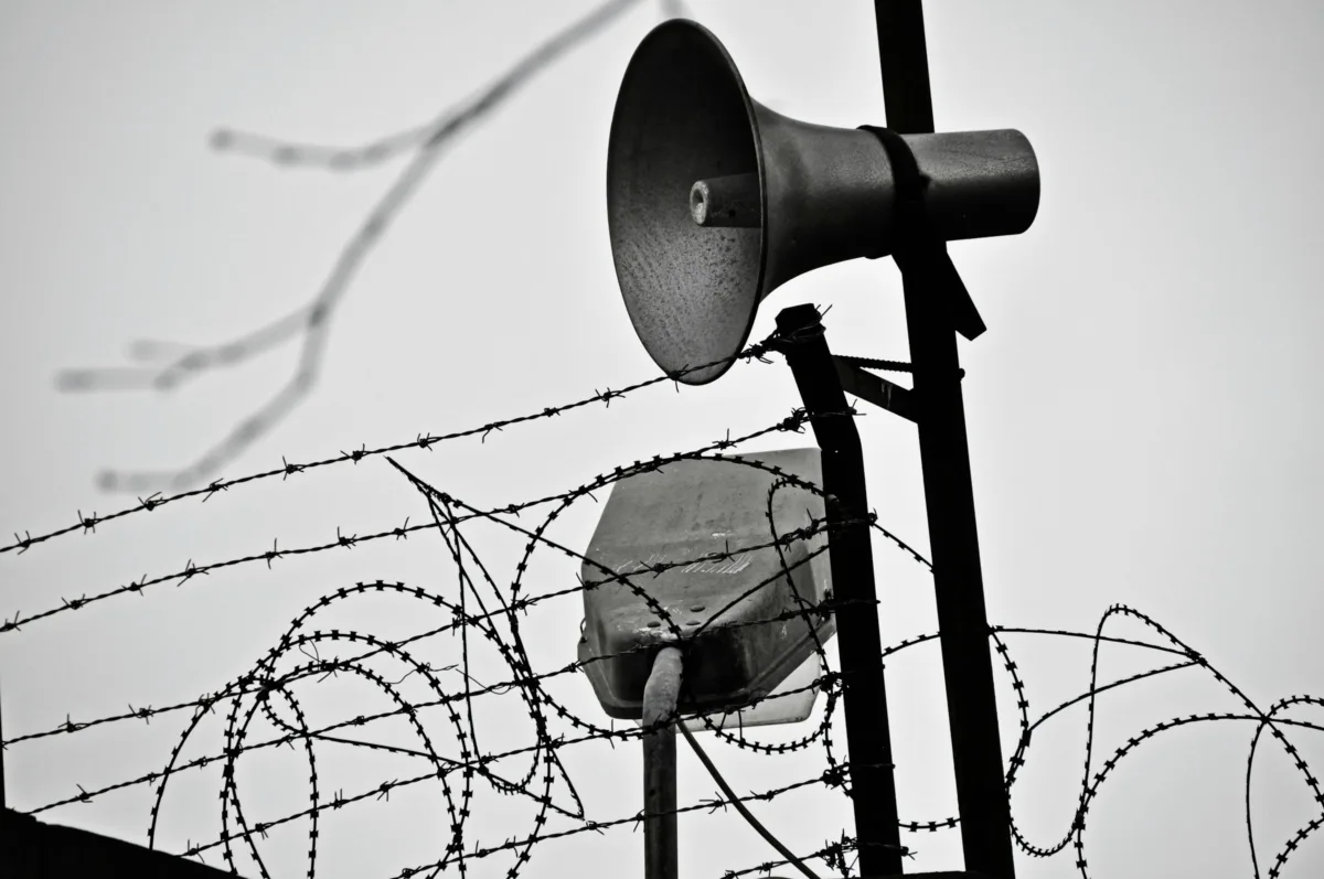 Speakers posted at the intersection of barbed wire and razor wire outside a prison