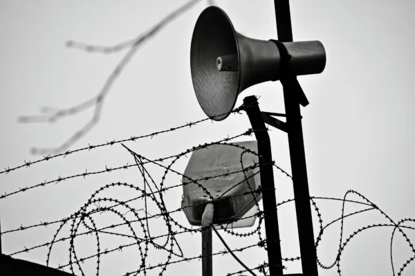Speakers posted at the intersection of barbed wire and razor wire outside a prison