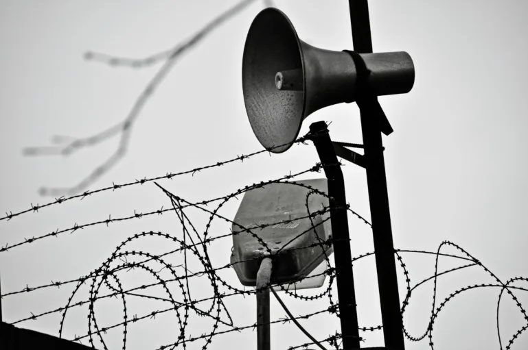 Speakers posted at the intersection of barbed wire and razor wire outside a prison