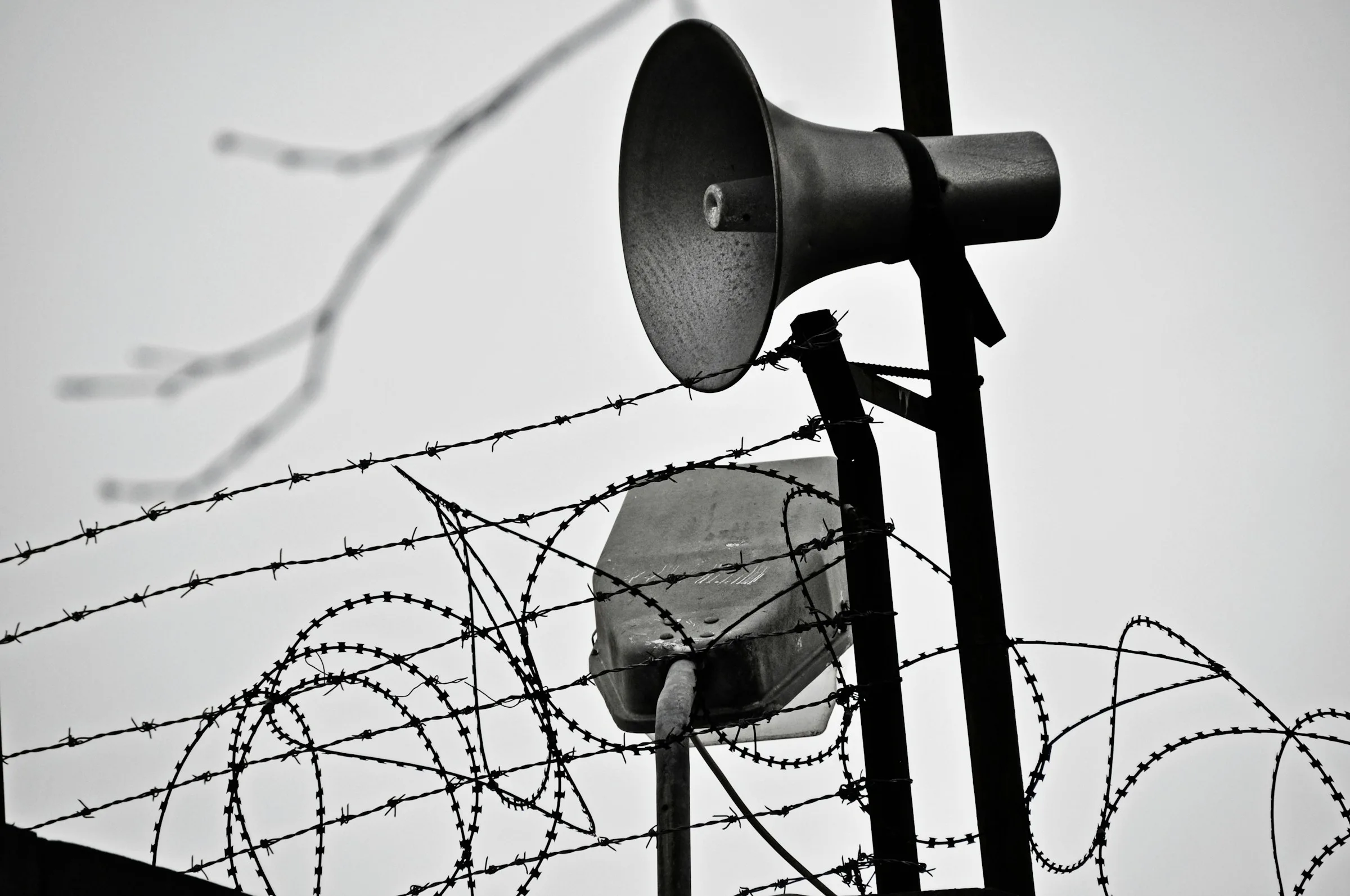 Speakers posted at the intersection of barbed wire and razor wire outside a prison